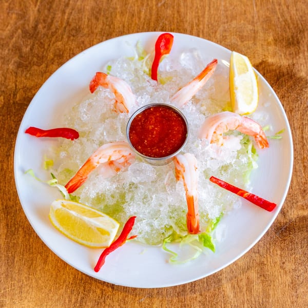 Shrimp cocktail with red sauce, lemon wedges, and red peppers on a bed of ice.