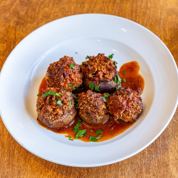 Five stuffed mushrooms with breading and parsley in a red sauce on a white plate.