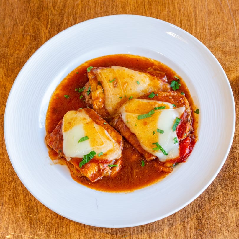 Three chicken parmesan cutlets with melted mozzarella and red sauce, garnished with parsley.
