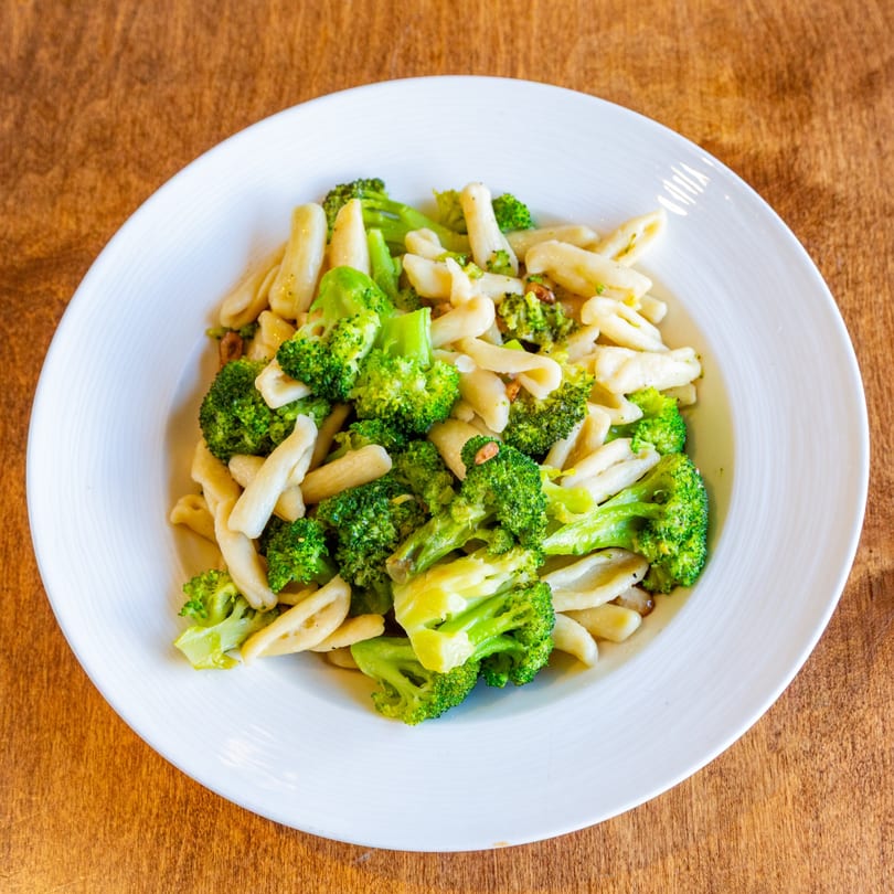 A white plate filled with cavatelli pasta and bright green broccoli florets on a wooden table.