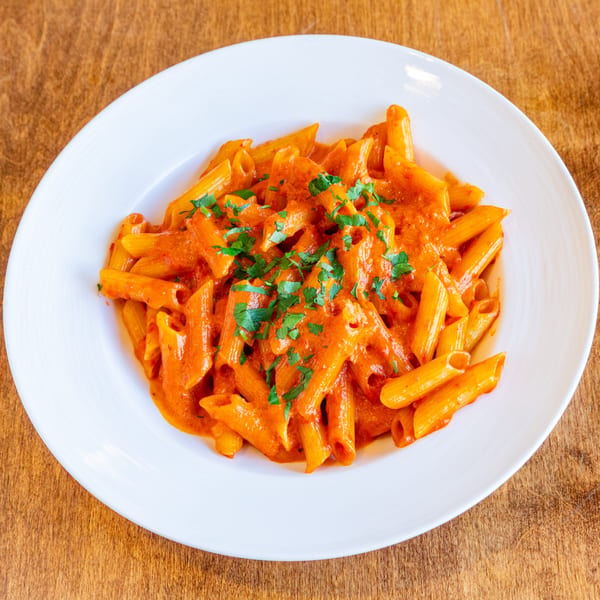 Penne pasta in a creamy red sauce, garnished with fresh parsley, served on a white plate.
