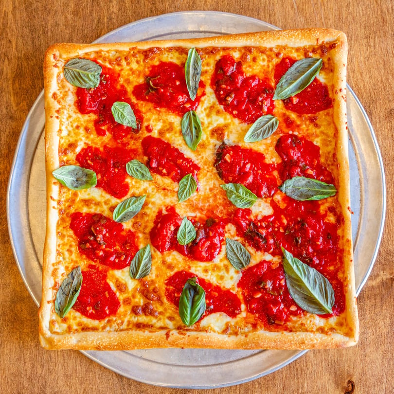 Square San Vito's pizza with melted cheese, dollops of red sauce, and fresh basil leaves.