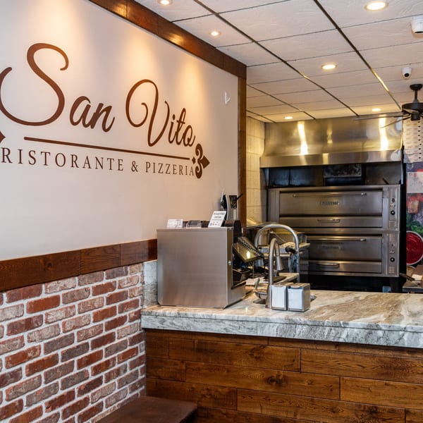 San Vito's Ristorante & Pizzeria sign above a counter with pizza ovens in the background.