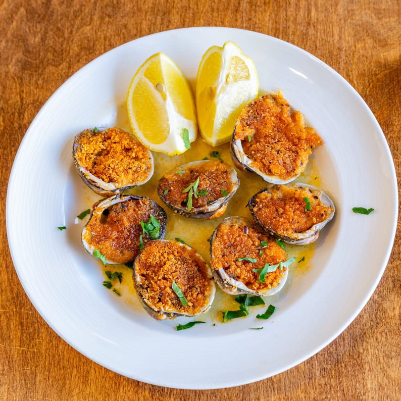 Baked clams with breadcrumbs and parsley, served with lemon wedges on a white plate.