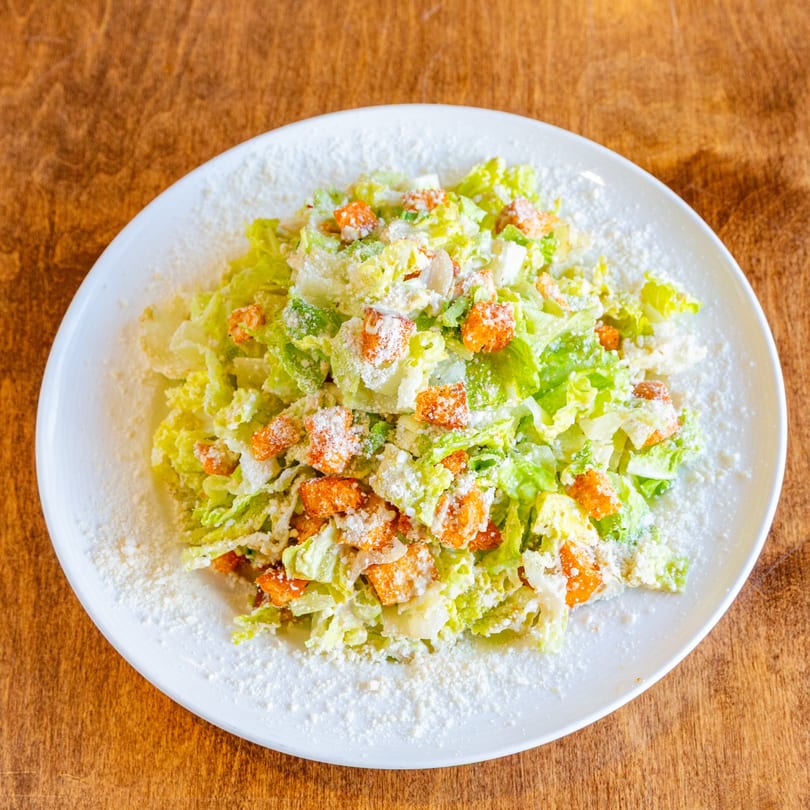 A San Vito's Caesar salad with crisp lettuce, croutons, and grated Parmesan cheese on a white plate.
