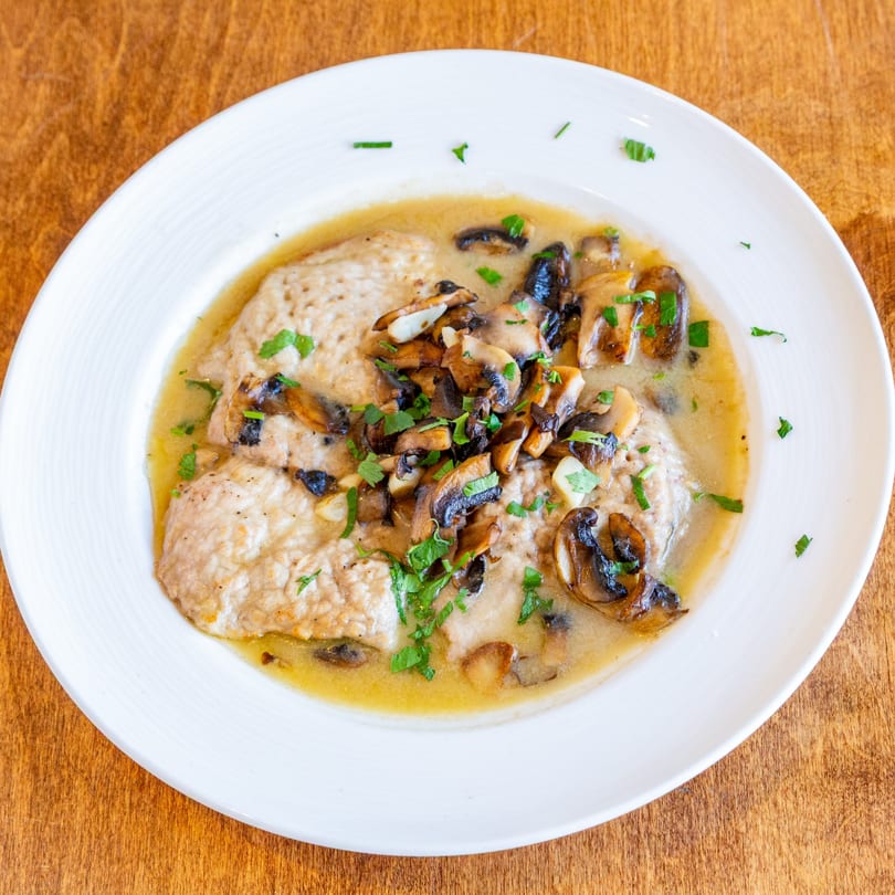 San Vito's chicken and mushroom dish in a creamy sauce, garnished with parsley on a white plate.