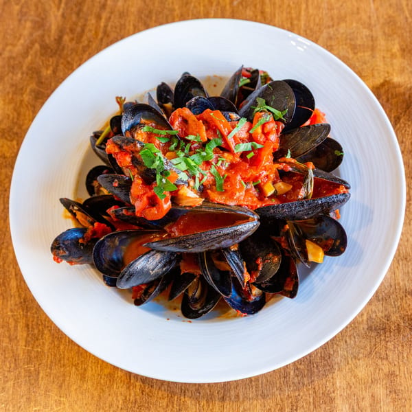 Steamed mussels in a rich red tomato sauce, garnished with fresh parsley, served on a white plate.