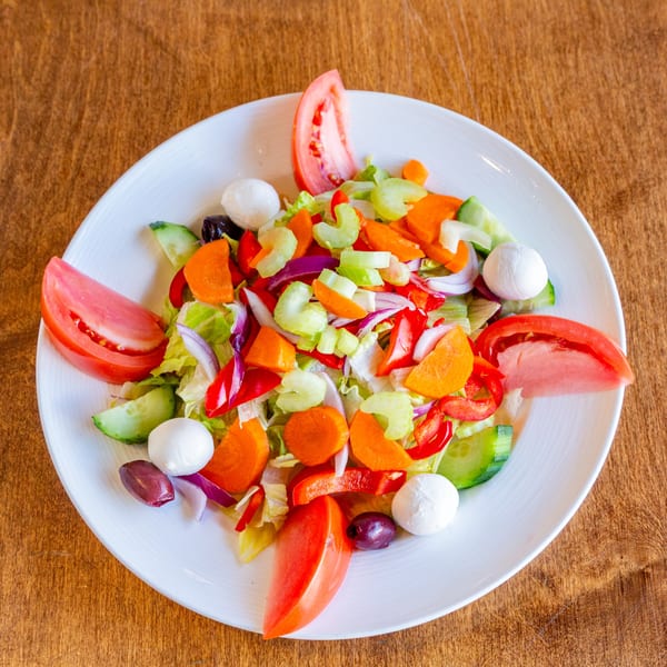 Colorful garden salad with tomatoes, mozzarella, olives, and mixed vegetables on a white plate.